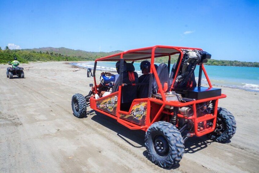 A red off-road vehicle on a sandy beach with a clear blue sky and distant hills. 2