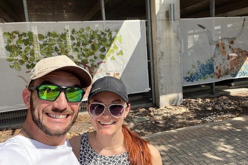 Twee mensen maken een selfie met een muurschildering van een boom en een koe op de achtergrond. 3