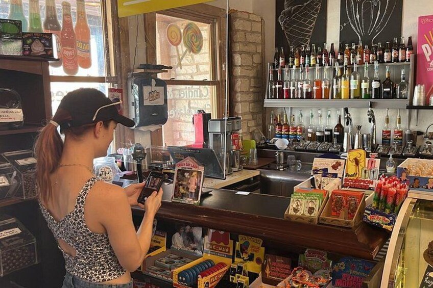 Een vrouw bij een bar met een smartphone, omringd door verschillende snacks en een keuze aan alcoholische dranken. 1