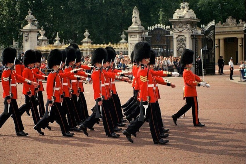 A group of guards in red uniforms marching in formation. 2