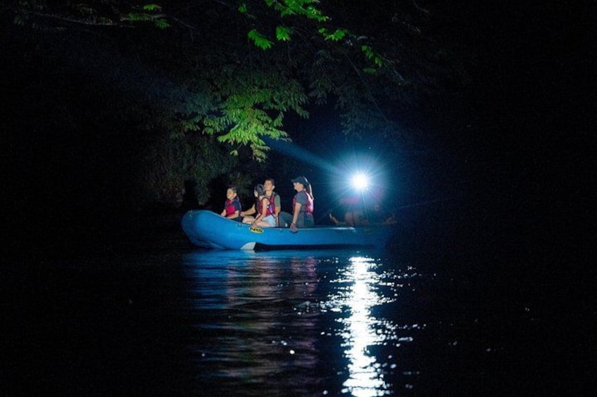 A group of people in a blue raft on a body of water at night, illuminated by a light source. 3
