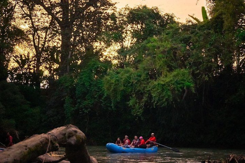 A group of people in a blue raft on a river surrounded by dense forest. 2
