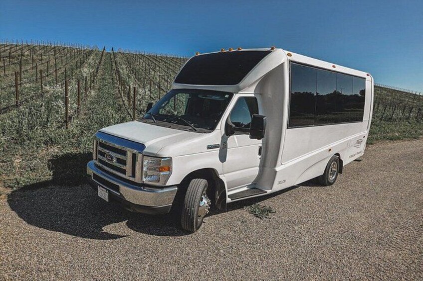 A white RV parked on a gravel road with a vineyard in the background. 2