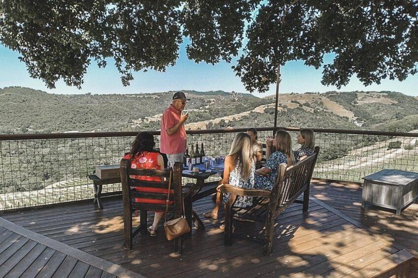 A group of people sitting on a wooden deck with a scenic view of hills in the background. 4
