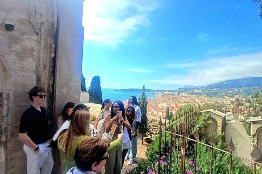 A group of people standing on a terrace overlooking a coastal cityscape with a clear sky. 5