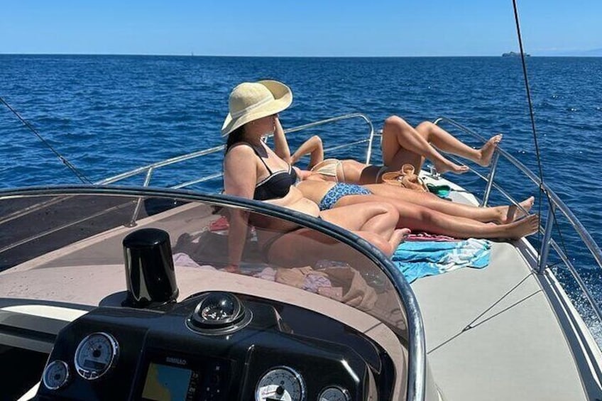 Twee personen zonnen op een boot, met een heldere blauwe zee op de achtergrond. 1