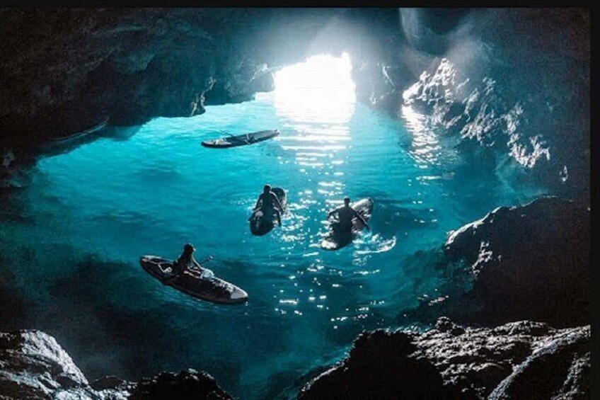 Una grotta con acqua cristallina blu, una barca e una persona che nuota. 2