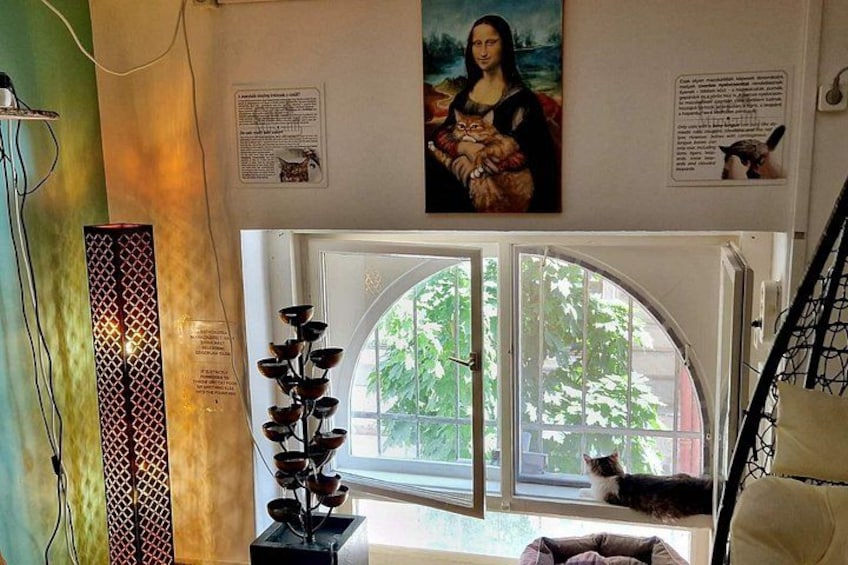 Una habitación con un ventanal grande, un cuadro de la Mona Lisa y un gato sentado junto a la ventana. 5