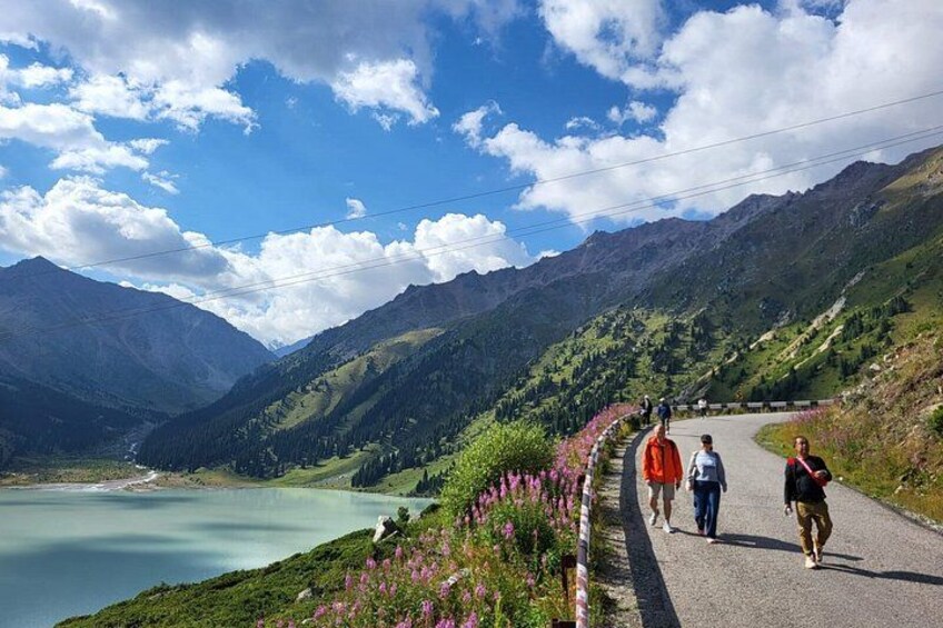 Une route de montagne avec un lac, des randonneurs et un ciel dégagé. 2