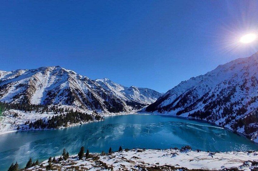 A snow-covered mountain range, a turquoise lake, and a clear blue sky. 4