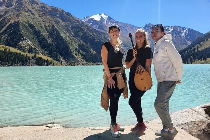 Three people standing by a turquoise lake with mountains in the background. 2