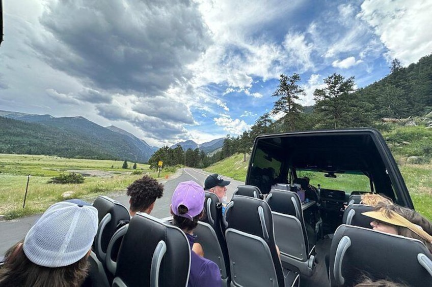 A vehicle with passengers seated inside, traveling on a road surrounded by mountains and greenery. 4