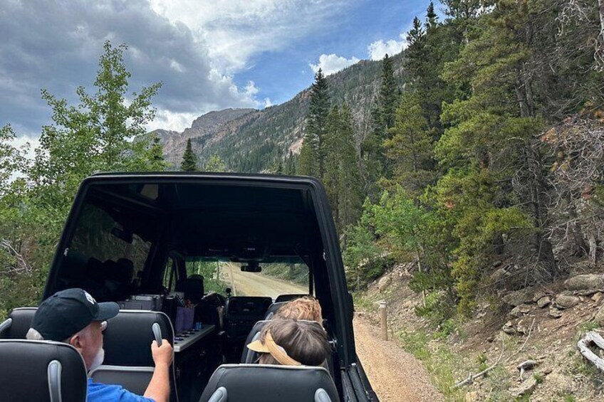 A vehicle on a dirt road surrounded by forested mountains. 5
