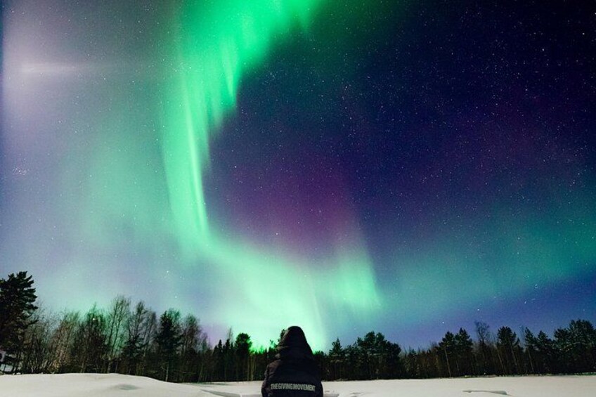 Una persona sentada sobre la nieve observando las auroras boreales. 3