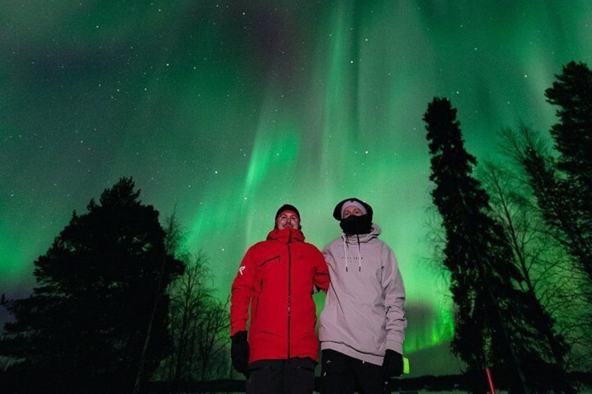 Dos personas de pie bajo una aurora boreal verde. 5