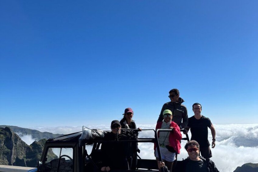 Un groupe de personnes se trouve à bord d’un véhicule tout-terrain en montagne, avec un ciel dégagé et des nuages en arrière-plan. 2