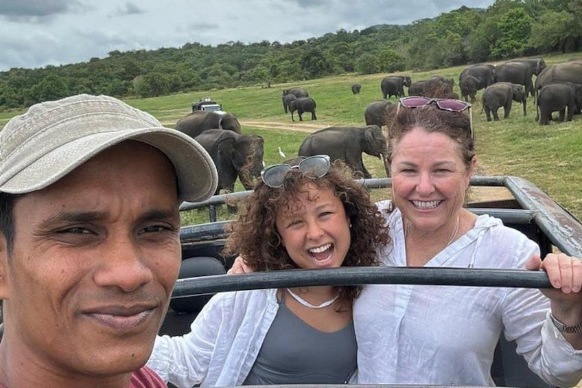 A group of people on a safari vehicle with elephants in the background. 1