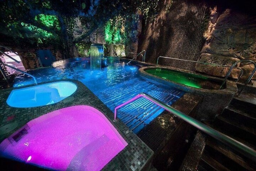 Una piscina al aire libre climatizada con una cascada, rodeada de terreno rocoso y vegetación. 1