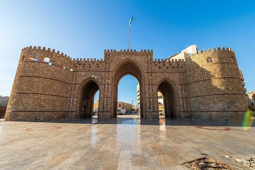 A stone archway with a flag, surrounded by a fortified wall. 2