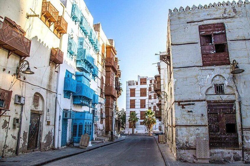 A narrow street lined with historic buildings, some with blue accents, and palm trees in the distance. 5