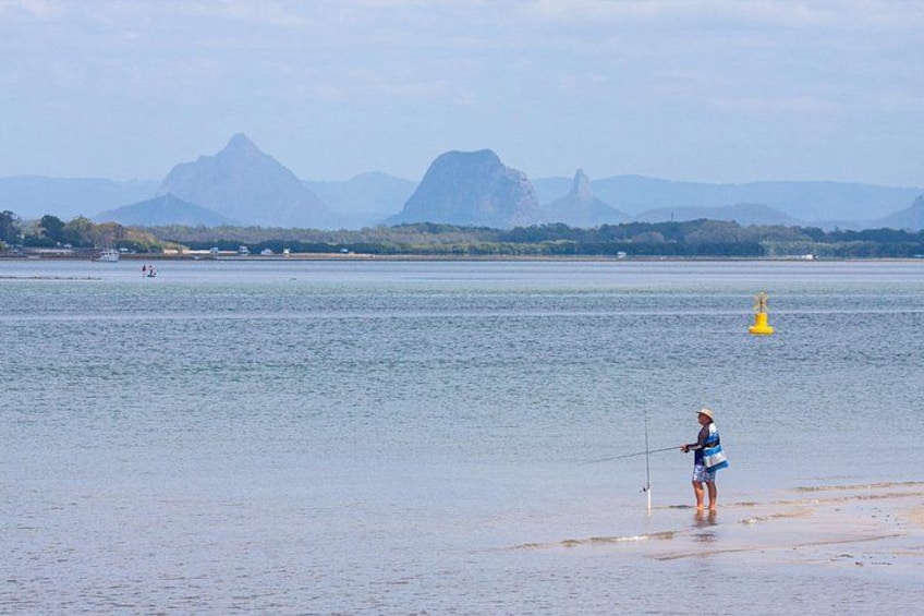 A person fishing by a calm body of water with mountains in the background. 2