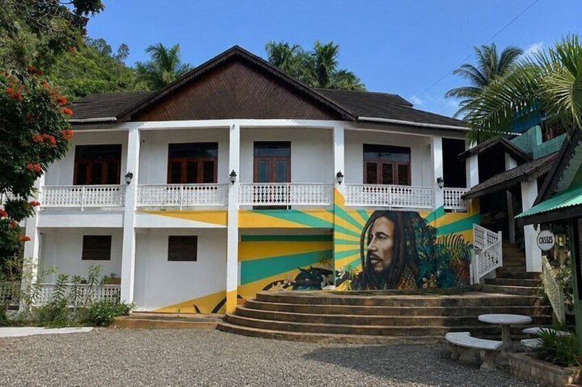A two-story building with a mural on the side, a balcony, and a staircase leading to the entrance. 1