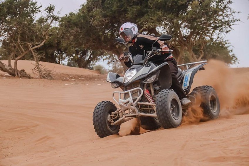 A person riding an ATV on a sandy terrain with sparse vegetation. 1