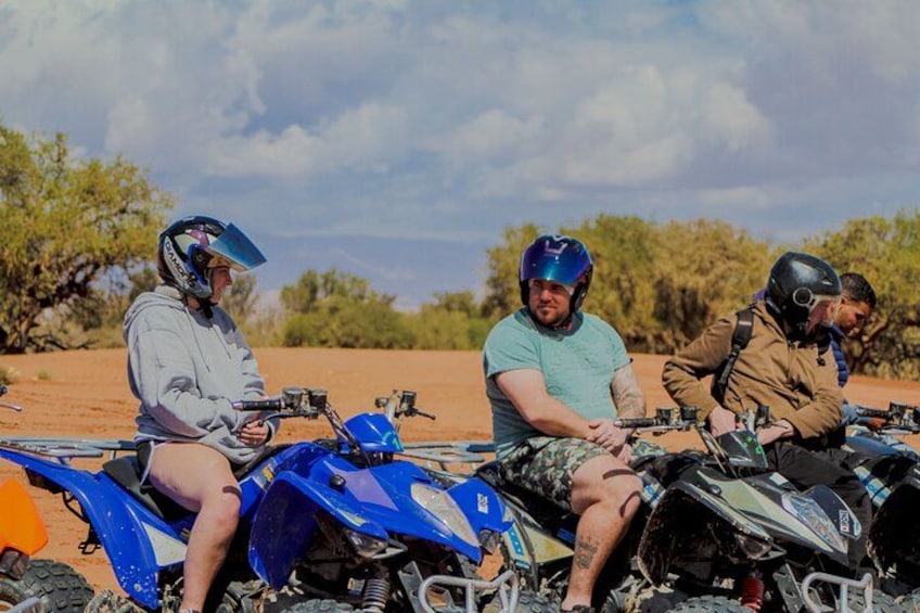 Three people sitting on off-road vehicles in a desert landscape with sparse vegetation. 2