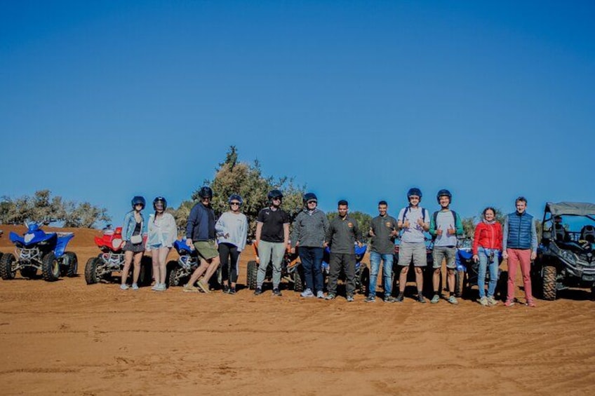 A group of people standing on a sandy terrain with off-road vehicles in the background. 4