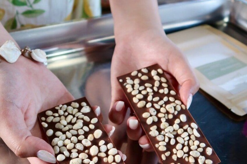 Deux mains tenant des tablettes de chocolat rectangulaires parsemées d’éclats de chocolat blanc. 2