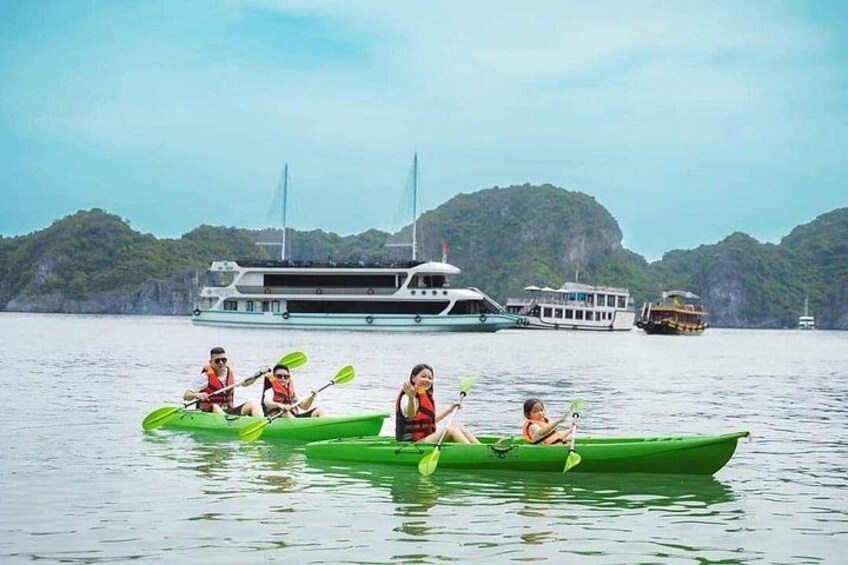 A group of people kayaking on calm water with a large boat and a mountainous landscape in the background. 3