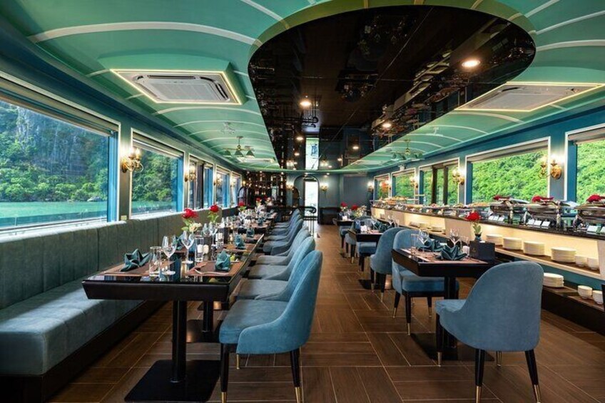 A restaurant with long tables, blue chairs, and large windows overlooking greenery. 1