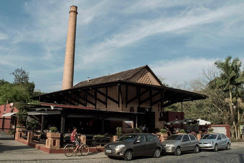Un edificio de ladrillo con una chimenea alta, un porche cubierto y coches estacionados. 3
