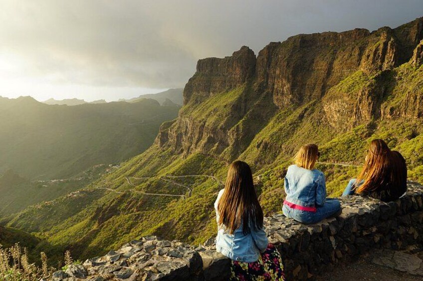 Three women sitting on a stone wall overlooking a mountainous landscape. 5