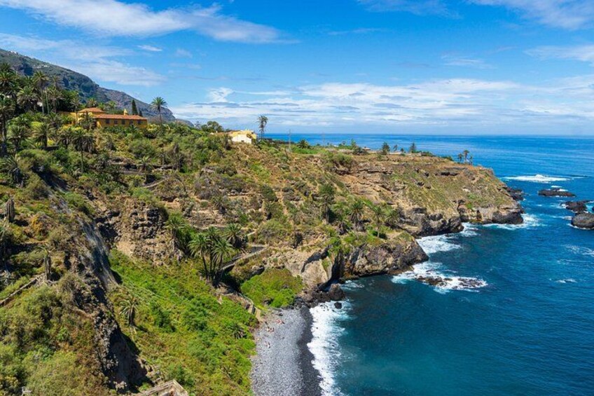 A coastal landscape with rocky cliffs, green vegetation, and a clear blue sea. 4