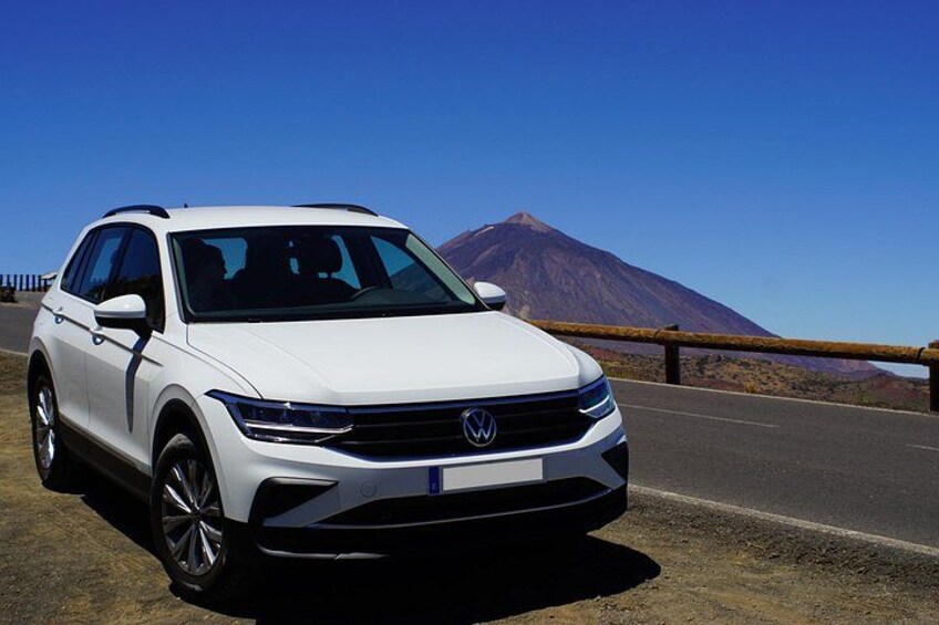 A white Volkswagen SUV parked on a road with a mountain in the background. 2