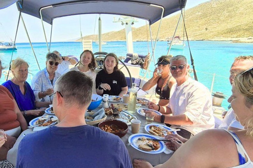Un grupo de personas cenando en un barco, con un mar azul cristalino y un paisaje montañoso al fondo. 2