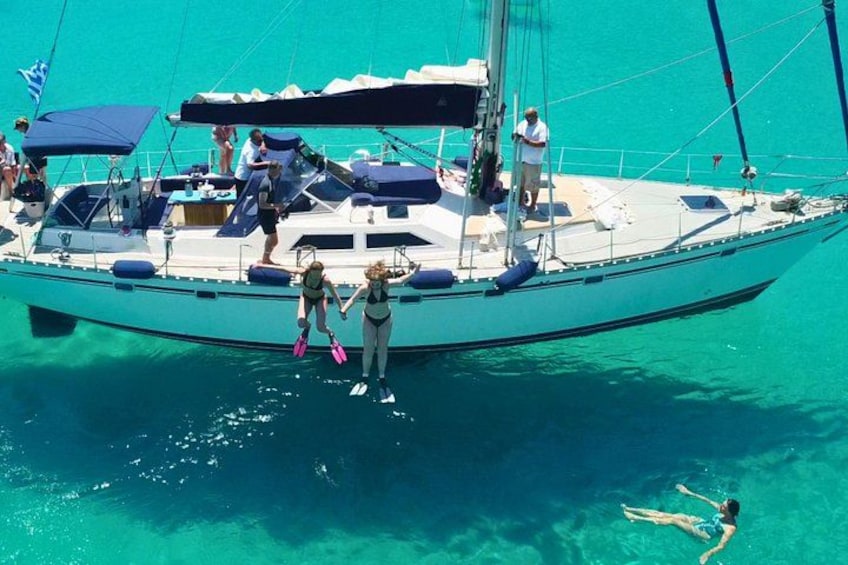 Un velero con gente en cubierta, una persona nadando en el agua y un mar azul y despejado. 4