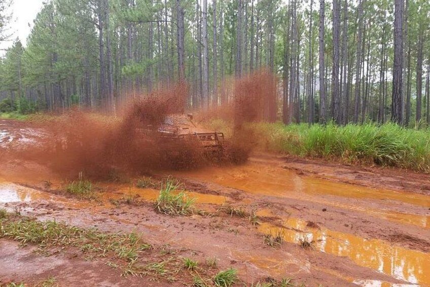 Een modderig offroad voertuig rijdt door een bebost gebied met modderig terrein en plassen water. 2