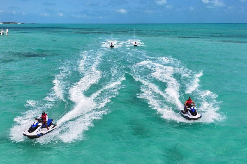 Three jet skis on turquoise water with wake trails, a clear sky, and a distant island. 2