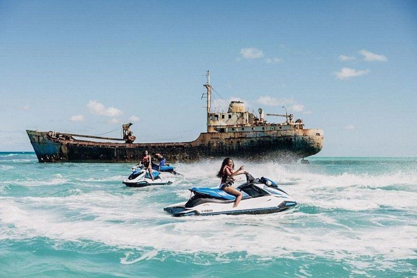 A person jet-skiing, a large rusted ship, and another person on a jet-ski in the ocean. 2