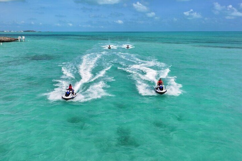 Three jet skis on turquoise water with wake trails, a clear sky, and distant land. 3