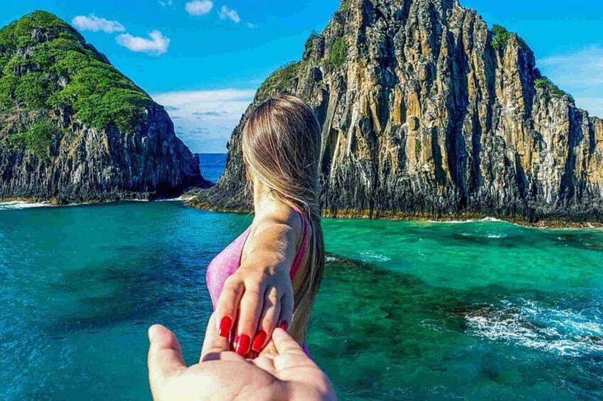 A hand holding a child's hand, facing a rocky coastline with clear blue waters. 1
