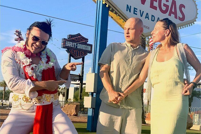 A man in a Hawaiian shirt and lei, a woman in a yellow dress, and a man in a white shirt standing in front of a Harley-Davidson sign. 2