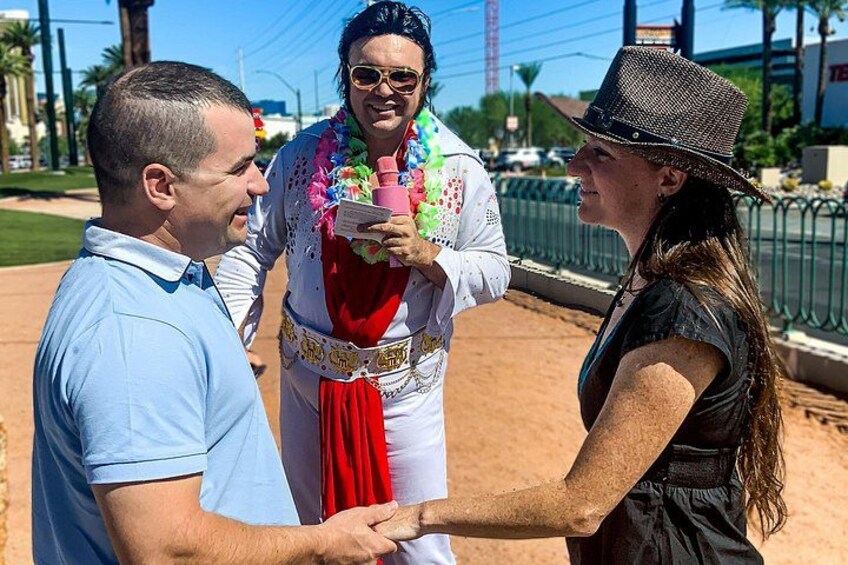 Three people in a casual outdoor setting, one person wearing a white outfit with a red scarf and holding a pink bottle, another in a blue shirt, and the third in a black dress. 4