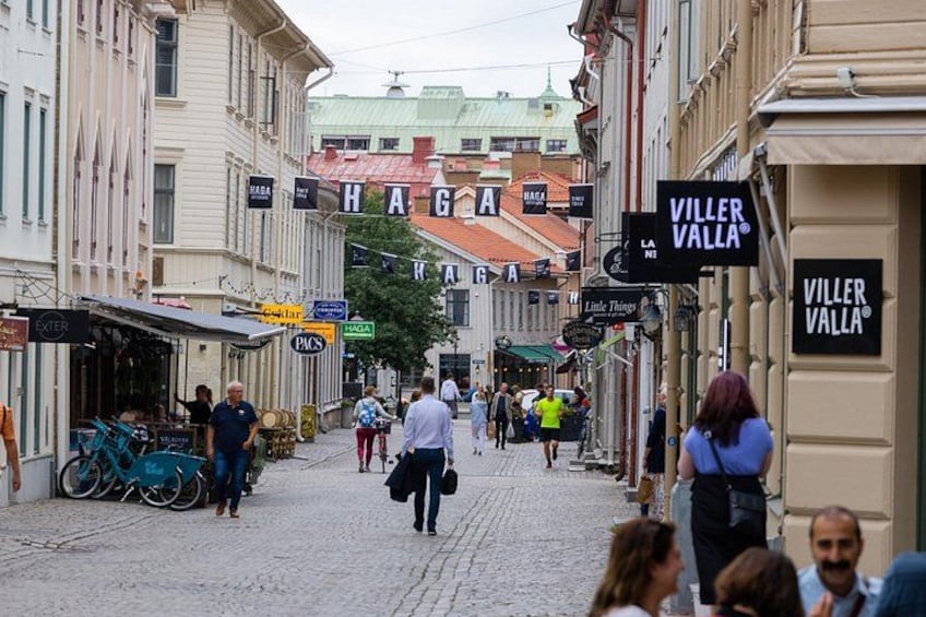 Una strada acciottolata fiancheggiata da negozi e insegne, tra cui si leggono 'VILLER VALLA' e 'HAGA'. 3