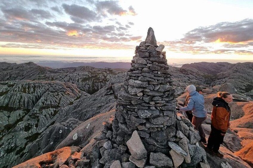 A rocky landscape with a stone cairn and hikers in the background. 1