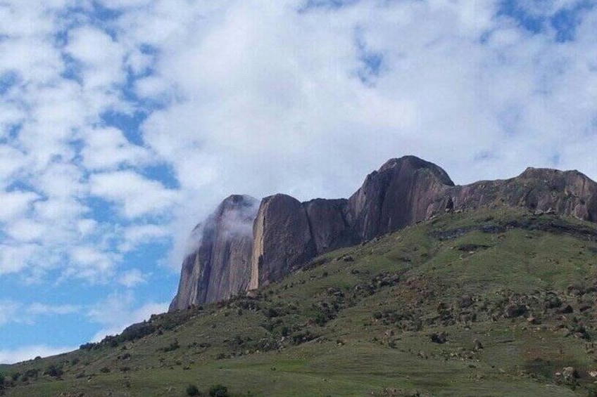 A mountainous landscape with a prominent rock formation and a grassy hill. 3