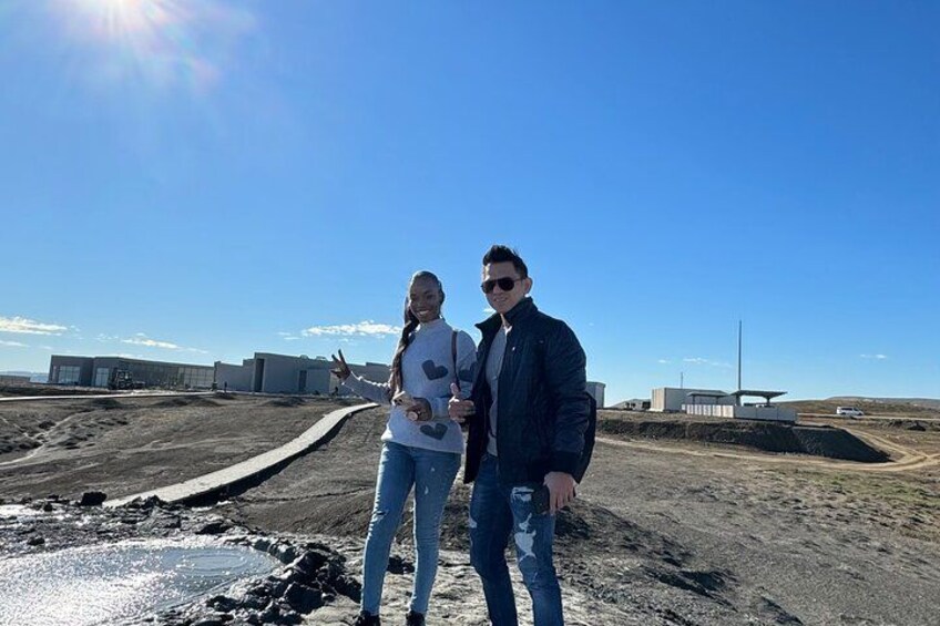 Twee personen staan op een onverharde pad met industriële gebouwen op de achtergrond. 5