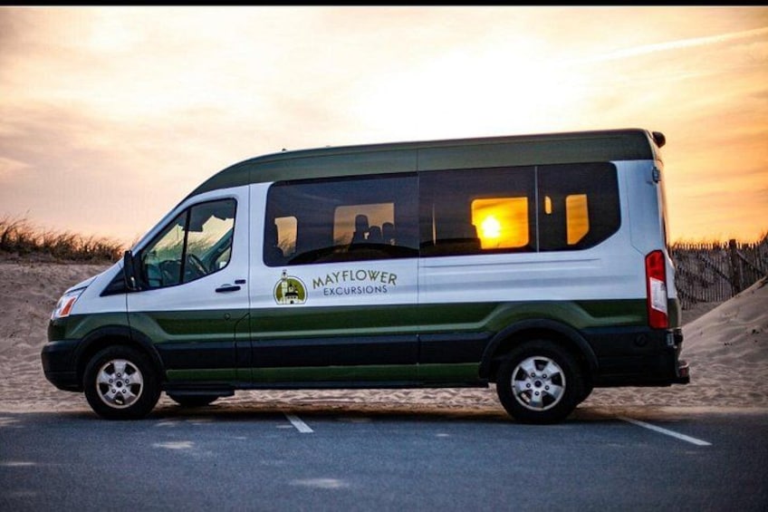 A white van with green stripes and the text 'Mayflower Excursions' on the side, parked on a road with a sunset in the background. 4